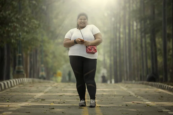 道路でスマート フォンを押しながらカメラで笑顔の肥満女性の画像 — ストック写真