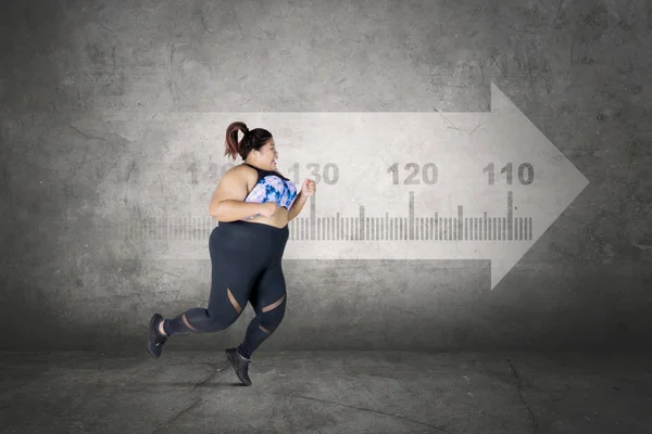 Picture of scared obese woman wearing sportswear while running with a measure tape shaped arrow