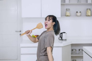 Şarkı ve mutfakta bir mikrofon olarak tahta bir spatula tutarken dans çekici genç kadını vurdu evde