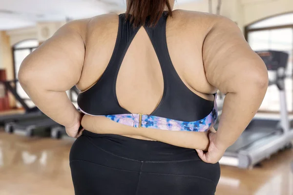 站在体育馆中心的年轻胖女人的背部视图显示她的腹部脂肪 — 图库照片