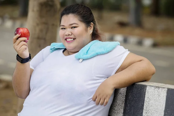 在公园里坐着一个新鲜苹果的快乐肥胖妇女的图片 — 图库照片