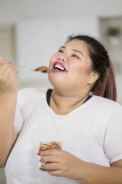 在家里用勺子享用巧克力奶油的肥胖妇女特写 — 图库照片