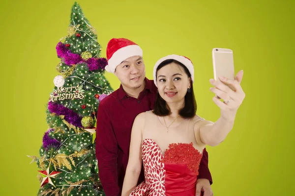 クリスマス ツリーの近くに立っている間スマート フォンを使用して Selfie 写真を撮る夫と美しい女性の写真 — ストック写真