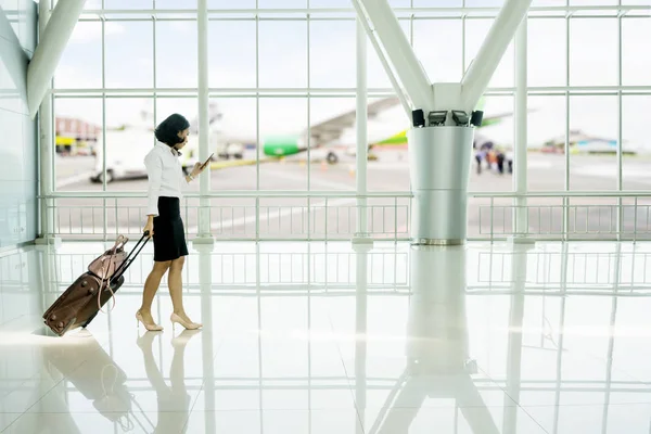 若いビジネス女性彼女の荷物を空港で歩きながら携帯電話を使用して — ストック写真