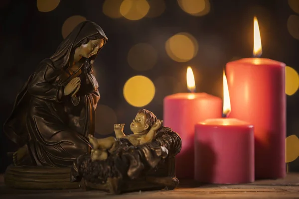 小雕像的婴儿耶稣与玛丽和燃烧蜡烛在桌子上 模糊闪闪发光的背景 — 图库照片