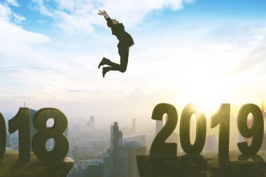 European businessman looks happy while leaping toward number 2019 in the cliff. Shot at sunrise time clipart