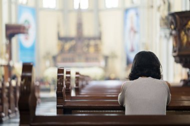 Rear view of religious woman praying to GOD while sitting in the church clipart
