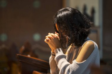 Side view of Asian woman praying to GOD while sitting in the church clipart