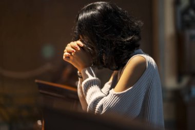 Side view of religious girl praying to GOD while sitting in the church clipart