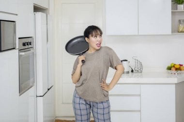 Mutfakta dans ederken bir kızartma tavası tutan genç kadın resmi