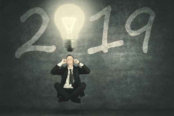Picture of European businessman thinking an idea while levitating under a bright bulb with number 2019