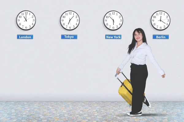 在不同国家时钟背景的机场行走时携带行李的女企业家 — 图库照片