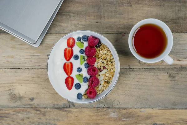 Cup of hot tea and fruit cereal with laptop on the wooden table