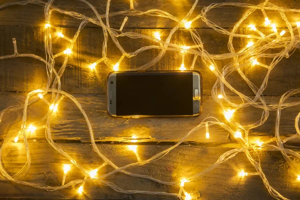 木製のテーブルにライトのメッシー クリスマスと携帯電話のトップ ビュー — ストック写真