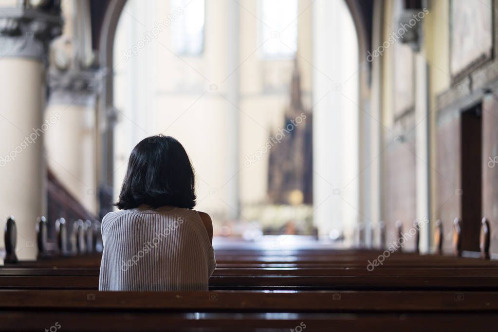 Rear view of devout woman sitting in the church while praying to the GOD