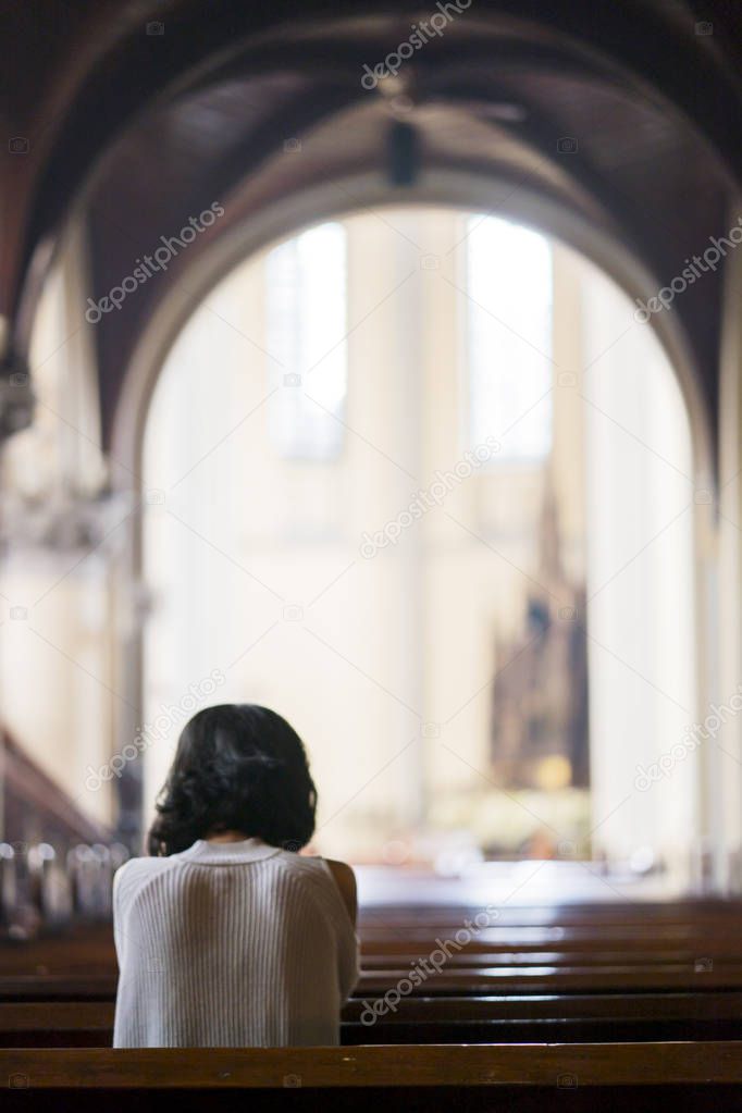 Rear view of young woman sitting in the church while praying to the GOD 