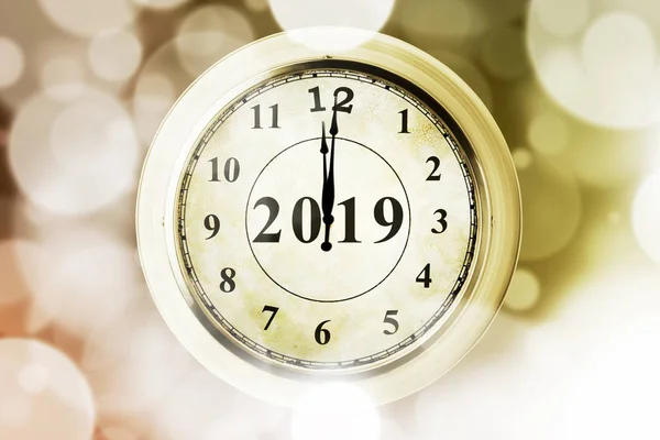 Image of golden clock with twelve o'clock and number 2019. Shot with blurred twinkling light background