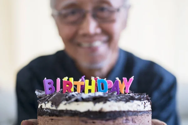 スタジオでバースデー ケーキをカラフルなろうそくを示す幸せな老人 — ストック写真