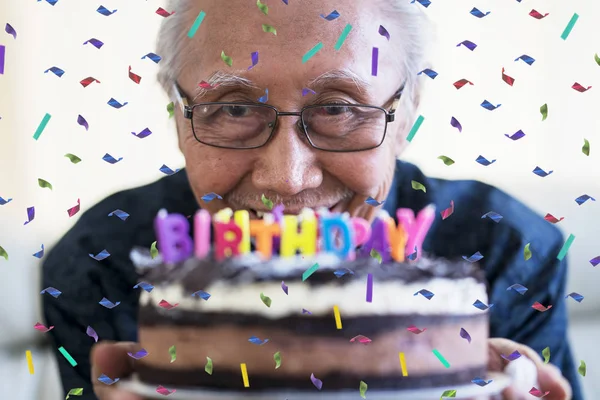 カラフルなキャンドルと紙吹雪で誕生日ケーキを持って満足している年配の男性を振りかける — ストック写真