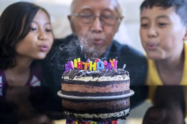 幸せな年配の男性と彼の孫の誕生日を祝って ケーキの誕生日の蝋燭を一緒に吹く — ストック写真