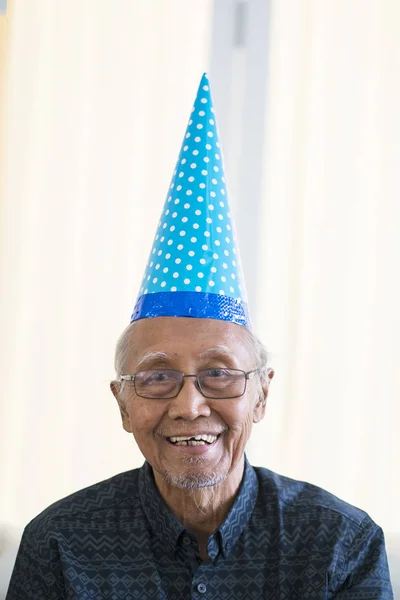 Portrait of old man smiling at the camera while wearing birthday hat at home