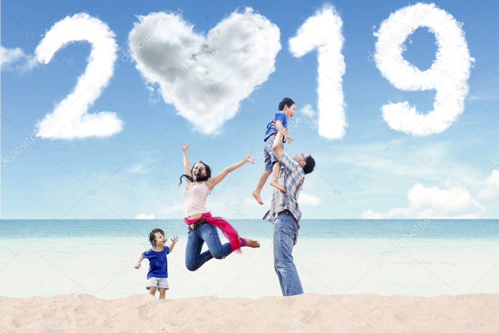 Portrait of Asian family having fun in the beach with clouds shaped heart and numbers 2019 in the sky