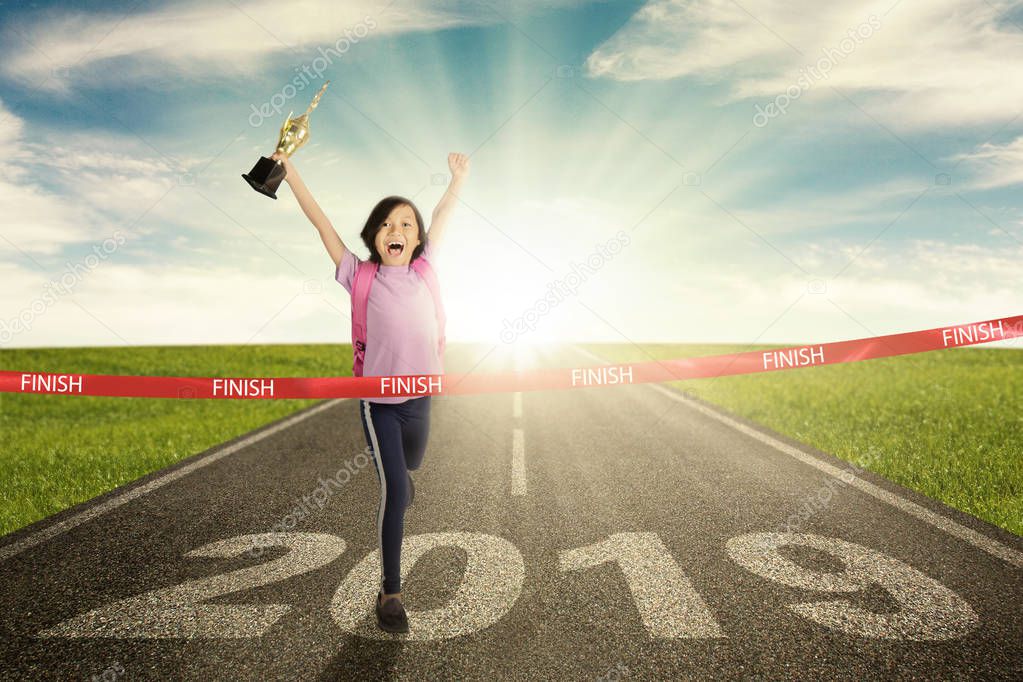 Picture of happy school girl  is carrying a trophy while crossing the success line with number 2019 on the road