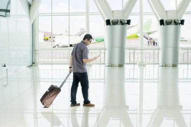 Havaalanı terminal yürürken bir akıllı telefon kullanan Asyalı adam
