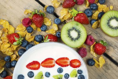 Sağlıklı kahvaltı kavramı. Bir kase yoğurt çilek, böğürtlen, ahududu, kivi ve tahta masada Mısır gevreği closeup