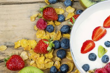 Sağlıklı kahvaltı kavramı. Bir kase yoğurt ve tahta masada Mısır gevreği ile taze çilek