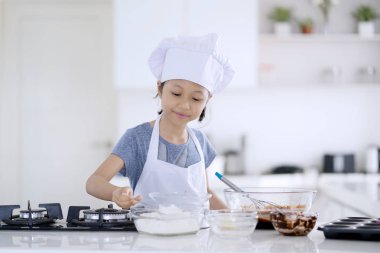 Güzel küçük bir kız evde mutfakta kurabiye hamuru un, yumurta ve kase çikolata yapma