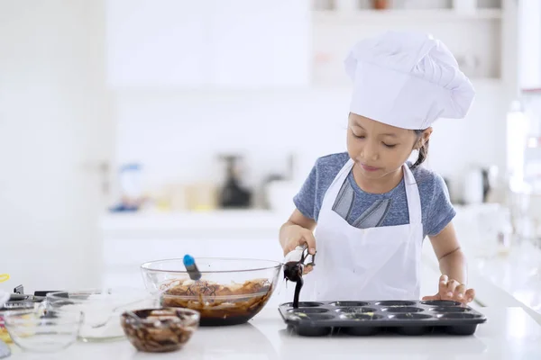 自宅のキッチンでクッキーを作るためのかわいい小さな女の子金型のチョコレート生地を注ぐ — ストック写真