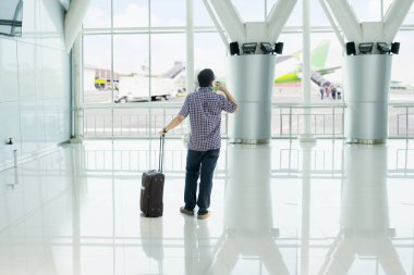 Arkadan görünüşü duran havaalanında cep telefonunda terminal konuşan bir genç adam