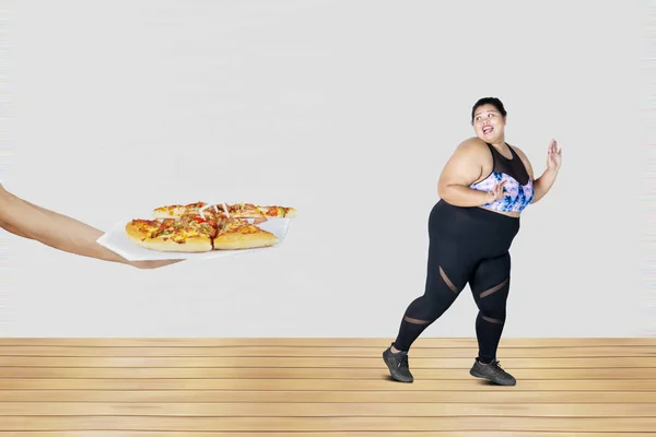 Picture of a scared fat woman running from tasty pizza offered. Diet concept