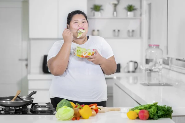 年轻胖女人的图片吃一碗美味的沙拉 而站在厨房 — 图库照片
