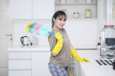 Resmi bir toz bezi fırça tutan ve mutfakta ayakta genç ev hanımı 
