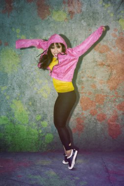 Genç kadın renkli beton arka plan ile stüdyoda hip hop dansı yaparken mutlu görünüyor