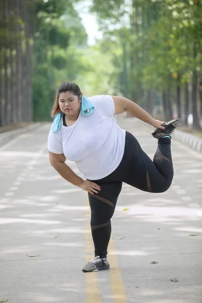 Portrait of fat female runner stretching legs before run on the road