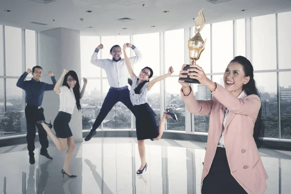 女经理在和她的团队站在一起庆祝他们在办公室的成功时举起了一个奖杯 — 图库照片