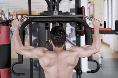 Spor merkezi fitness makine ile egzersiz yapan bir genç erkek arka görünümü