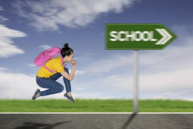 Kız öğrencinin okula hızlı hareket arka planda doğru çalışırken bir sırt çantası taşıyan yan görünüm