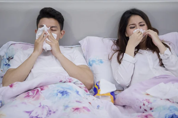 生病的年轻夫妇躺在床上用纸巾擦鼻子的肖像 — 图库照片