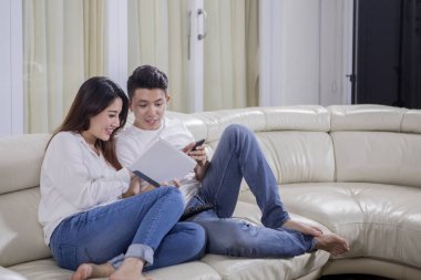Asya çift birlikte evde tablet ve cep telefonu kullanırken kanepede rahatlatıcı bir görüntü