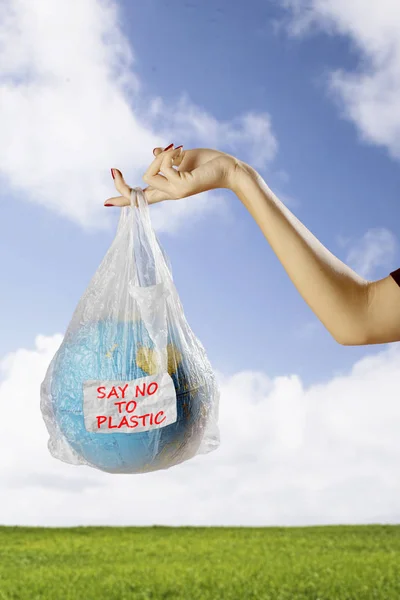 Close up of female holds an earth globe in a plastic bag with text of say no to plastic. Shot in the meadow
