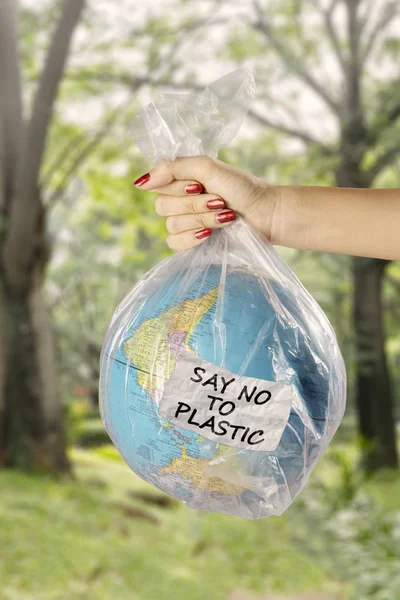 Concept of save earth from plastic waste pollution. Unknown woman holds a plastic bag with earth globe and text of say no to plastic