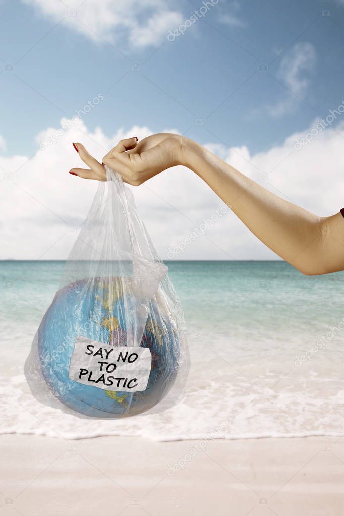 Close up of young woman hands holding an earth globe in a plastic bag with text of say no to plastic. Shot in the beach