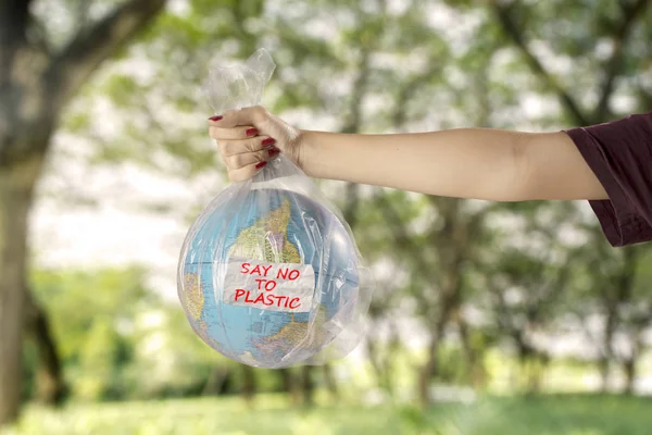 Concept of save earth from plastic waste pollution. Young woman with earth globe in a plastic bag and text of say no to plastic