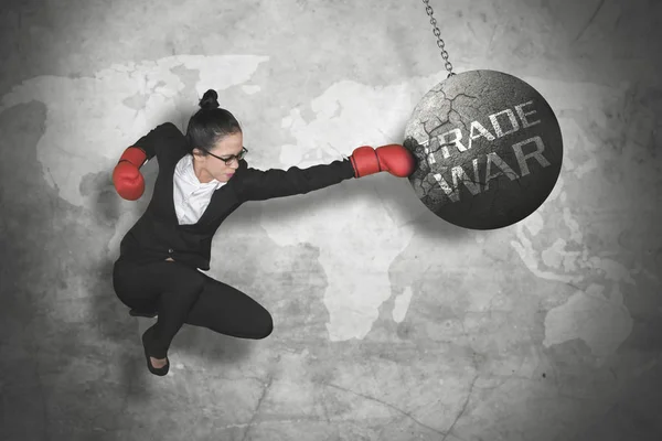 Image of female entrepreneur wearing boxing gloves while jumping and punching trade war text on the pendulum