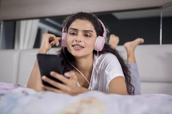 漂亮女孩的形象是躺在床上 用耳机和智能手机听到音乐 — 图库照片