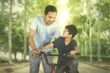 Küçük bir çocuk babası tarafından parkta Bisiklete binmeyi öğrenirken yardımcı oldu. Yaz anda vurdu